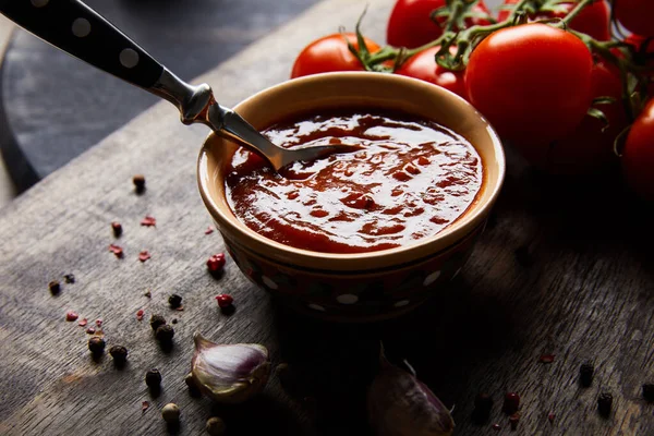 Köstliche Tomatensauce in Schüssel mit Löffel neben Tomaten und Gewürzen auf Holzbrett — Stockfoto