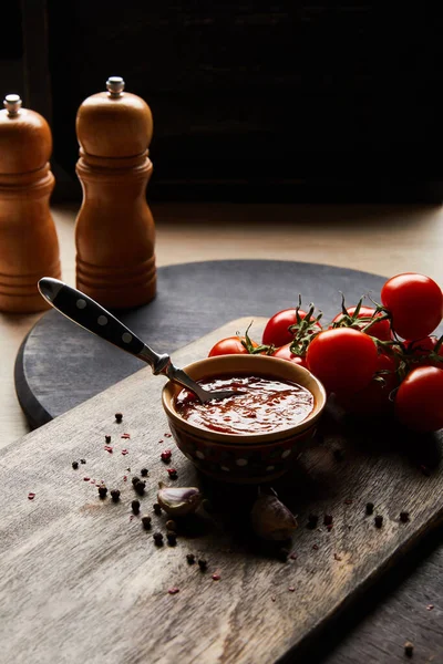 Délicieuse sauce tomate dans un bol avec cuillère près des tomates et des épices sur un plateau en bois — Photo de stock