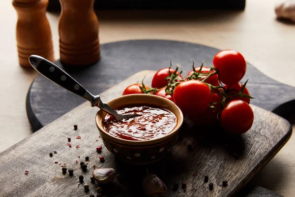 Focus selettivo di deliziosa salsa di pomodoro in ciotola con cucchiaio vicino a pomodori e spezie su tavola di legno — Foto stock