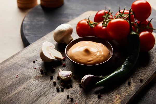 Вкусный соус в миске рядом с грибами, помидорами и специями на деревянной доске — стоковое фото