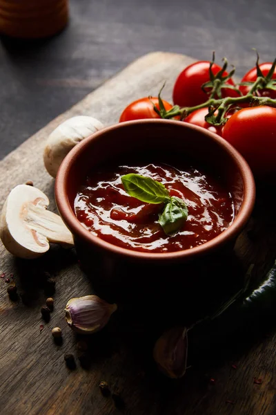 Delicious tomato sauce in bowl near mushrooms, tomatoes and spices on wooden board — Stock Photo