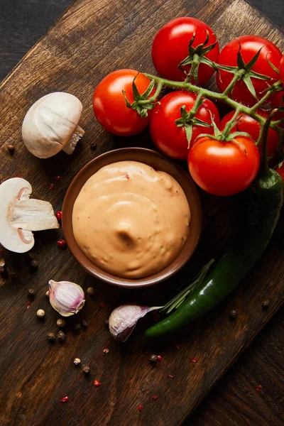 Top view of delicious sauce in bowl near mushrooms, tomatoes and spices on wooden board — Stock Photo