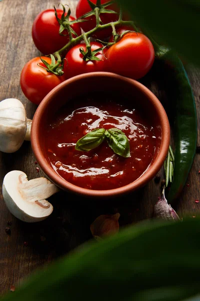 Foco seletivo de delicioso molho de tomate em tigela perto de cogumelos, tomates e especiarias em tábua de madeira — Fotografia de Stock
