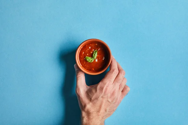 Vista dall'alto di mano maschile con deliziosa salsa di pomodoro in ciotola su sfondo blu — Foto stock