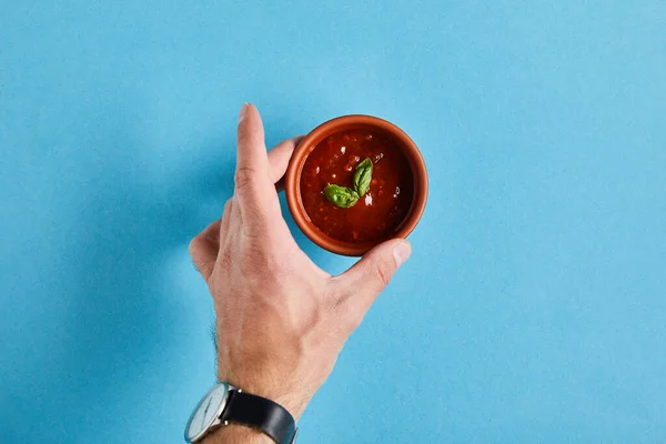 Top view of male hand with delicious tomato sauce in bowl on blue background — Stock Photo