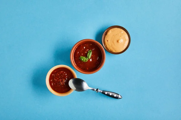 Вид сверху на вкусные соусы в мисках с ложкой на голубом фоне — стоковое фото