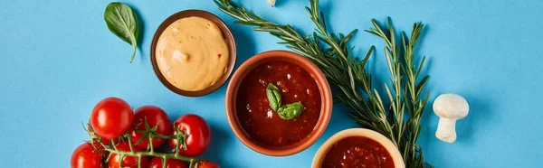 Vista superior de deliciosas salsas en cuencos cerca de verduras frescas maduras sobre fondo azul, plano panorámico - foto de stock