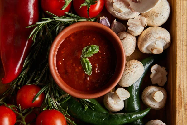 Ansicht von Tomatensauce mit Basilikumblättern in der Nähe von Kirschtomaten, grünen Chilischoten, Pilzen und Rosmarin — Stockfoto