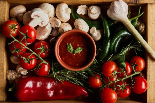 Top view of tomato sauce with basil leaves near cherry tomatoes, green chili peppers, mushrooms and rosemary in wooden box — Stock Photo