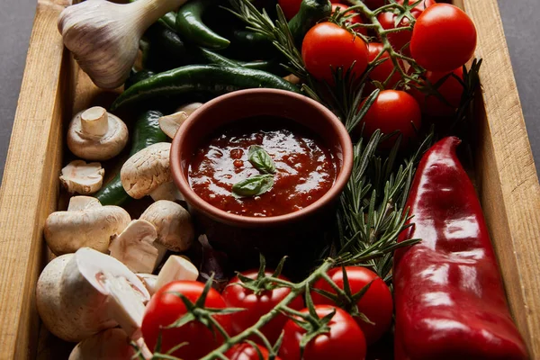 Foco seletivo de folhas de manjericão fresco em molho de tomate perto de cogumelos, tomates cereja vermelha, alecrim e pimentas em caixa de madeira — Fotografia de Stock