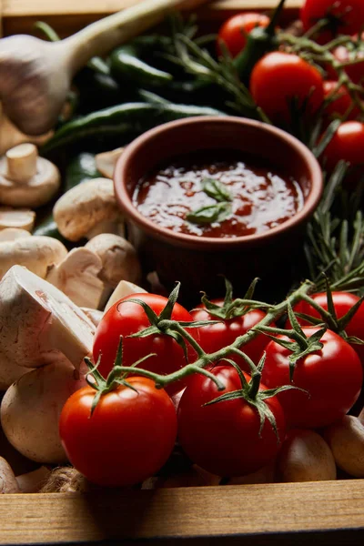 Selective focus of mushrooms, cherry tomatoes, tomato sauce near rosemary and green chili peppers in wooden box — Stock Photo