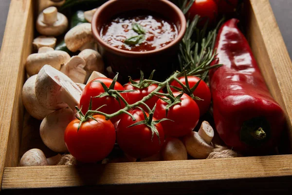 Селективний фокус вишневих помідорів, грибів, томатного соусу біля розмарину та червоного перець чилі в дерев'яній коробці — стокове фото