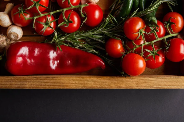 Top view of cherry tomatoes, mushrooms near rosemary and red chili pepper in wooden box on black — Stock Photo