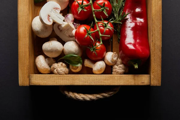 Ansicht von Kirschtomaten, Chilischoten, Champignons, Blumenkohl und Knoblauchzehen in der Nähe von Basilikumblatt und Rosmarin in Holzkiste auf schwarz — Stockfoto