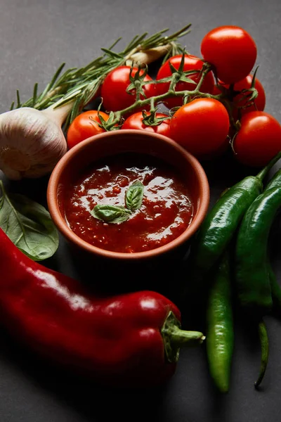 Tomates cherry maduros, ajo, salsa de tomate en un tazón, romero cerca de chiles sobre negro - foto de stock