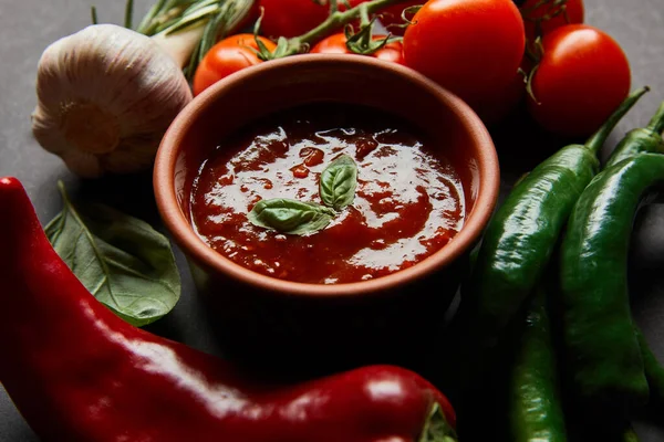 Primer plano de tomates cherry maduros, ajo, salsa de tomate en tazón y romero cerca de chiles sobre negro - foto de stock