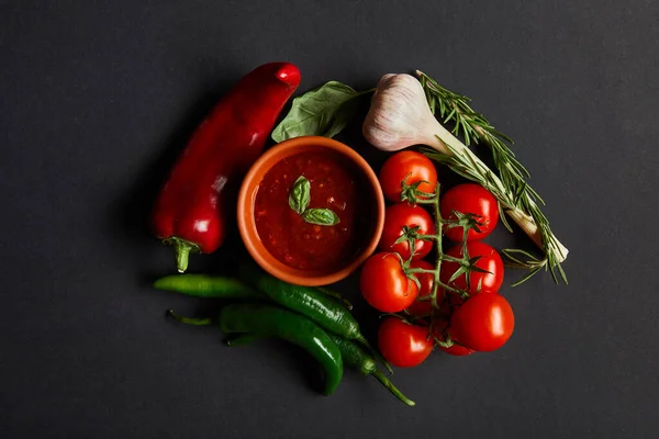 Vista superior de tomates cherry maduros, ajo, salsa de tomate en tazón y romero cerca de chiles sobre negro - foto de stock