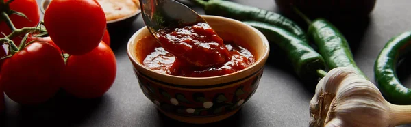 Conceito panorâmico de colher em molho de tomate saboroso perto de legumes maduros em preto — Fotografia de Stock