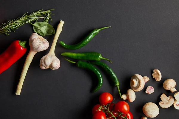 Blick von oben auf reife Kirschtomaten, Knoblauch, Rosmarin, Basilikumblätter, grüne Chilischoten und Champignons auf schwarz — Stockfoto