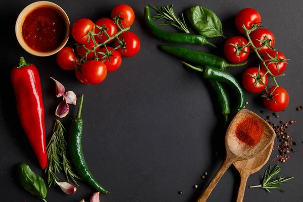 Flat lay with ripe cherry tomatoes, garlic cloves, rosemary, peppercorns, basil leaves and green chili peppers on black — Stock Photo