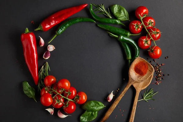 Flat lay with red cherry tomatoes, garlic cloves, rosemary, peppercorns, basil leaves and green chili peppers on black — Stock Photo