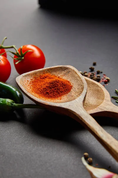 Enfoque selectivo de tomates cherry orgánicos, granos de pimienta, cucharas de madera con pimentón en polvo y chiles verdes en negro - foto de stock