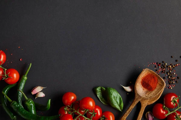 Blick von oben auf reife Kirschtomaten, Knoblauchzehen, frischen Rosmarin, Pfefferkörner, Basilikumblätter und grüne Chilischoten auf schwarz — Stockfoto