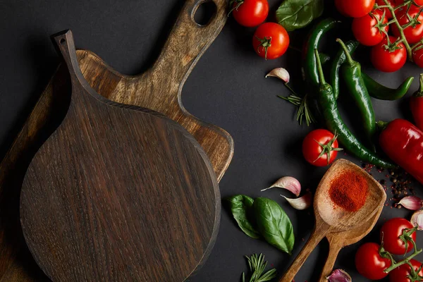 Top view of red cherry tomatoes, garlic cloves, rosemary, peppercorns, and green chili peppers near chopping boards on black — Stock Photo