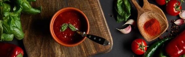 Horizontal crop of red cherry tomatoes, tomato sauce, peppercorns, herbs and green chili peppers near cutting board on black — Stock Photo