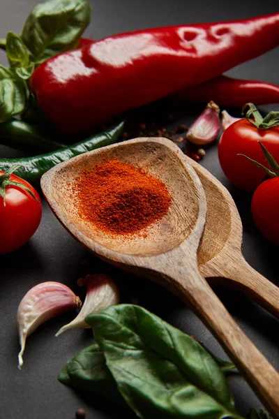 Selektiver Fokus auf reife Kirschtomaten, Kräuter und Chilischoten in der Nähe von Löffeln mit Paprikapulver auf schwarzem — Stockfoto