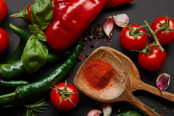 Vue de dessus des tomates cerises, des herbes fraîches et des piments près des cuillères avec de la poudre de paprika sur noir — Photo de stock