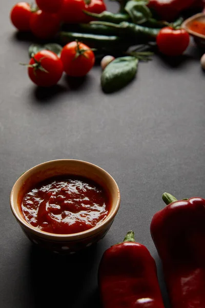 Top view of bowl with tomato sauce near spicy chili peppers on black — Stock Photo