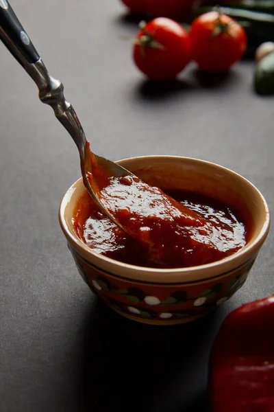 Nahaufnahme von Löffel in Schüssel mit Tomatensauce auf schwarz — Stockfoto