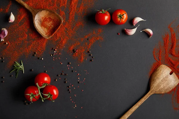 Vue de dessus des tomates cerises savoureuses et des herbes fraîches près des cuillères avec de la poudre de paprika sur noir — Photo de stock