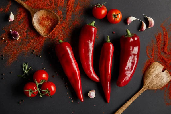 Vista superior de pimentas picantes, tomates cereja e alecrim fresco perto de colheres com páprica em pó em preto — Fotografia de Stock