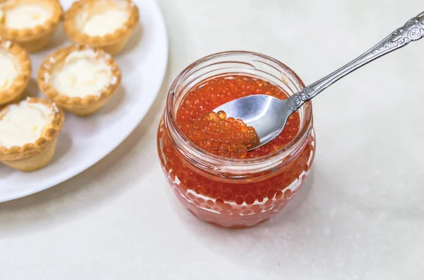 Segurando uma tigela de vidro com caviar vermelho. Colher em caviar vermelho. Frutos do mar caros, iguarias . Imagem De Stock