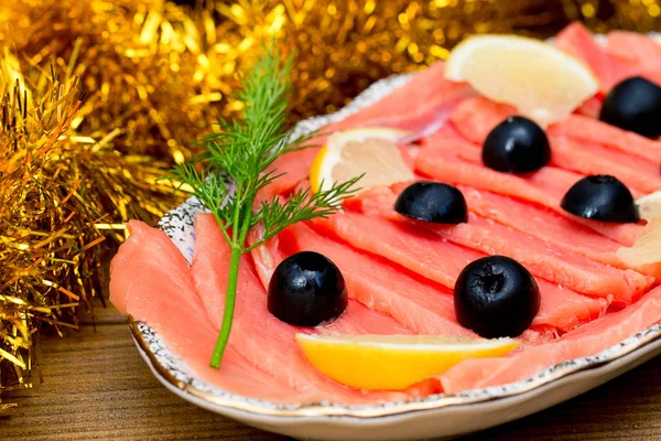 sliced red fish salmon greens lemon black olives on plate, wooden brown background, top view, food serving