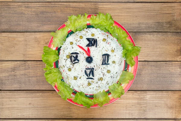 The Christmas salad rice olives greens peas - concept New year clock face, midnight, brown wooden background. Stock Picture