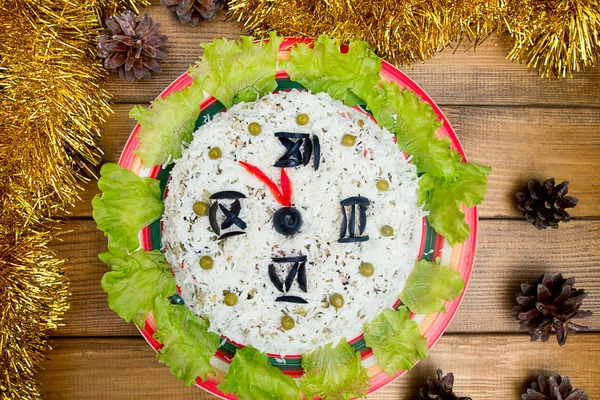 The Christmas salad rice olives greens peas - concept New year clock face, midnight, brown wooden background spruce cones tinsel on the table. Stock Photo