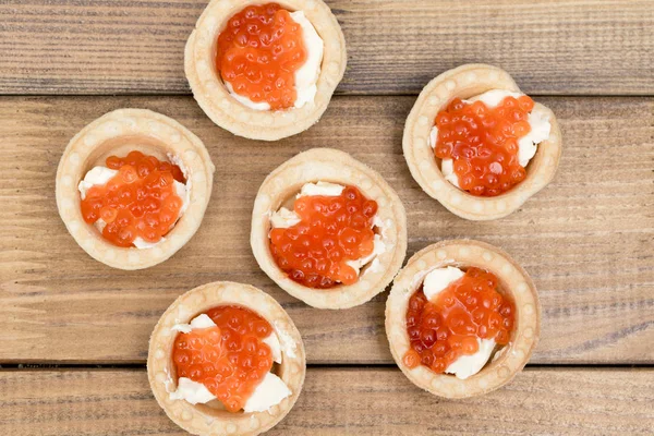 Die verschiedenen Törtchen mit rotem Kaviar und Butter auf hölzerner brauner Tischplatte Stockbild