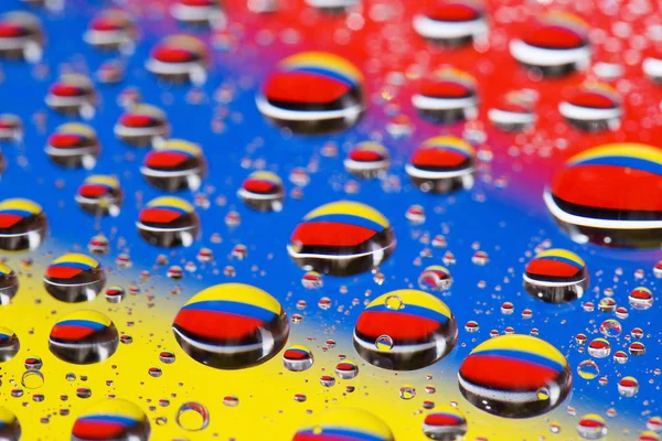 O fundo azul-amarelo-vermelho abstrato de gotas de água em vidro com macro verde de reflexão — Fotografia de Stock
