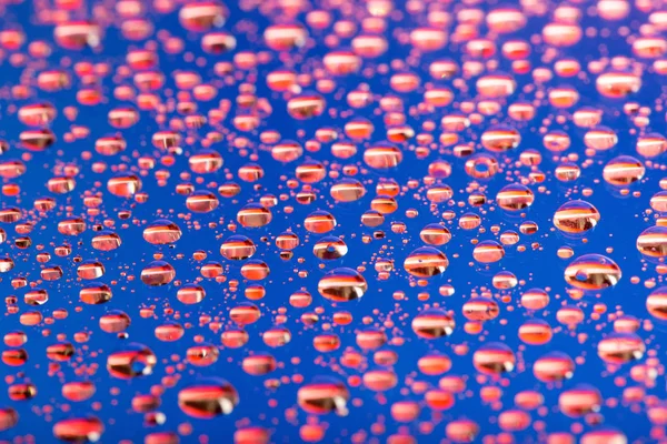 El fondo Abstracto azul-rojo de las gotas de agua sobre el cristal con la reflexión verde macro —  Fotos de Stock