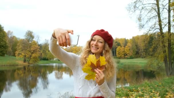 Chica feliz con hojas de arce de otoño haciendo selfie con teléfono móvil en el parque — Vídeo de stock