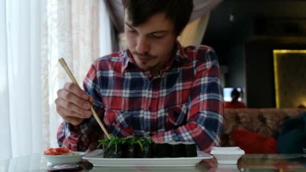 Молодой человек ест суши в японском ресторане — стоковое видео