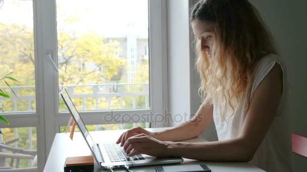 Leuke jonge vrouw praten met vrienden via mobiele telefoon terwijl u werkt op een laptop, en vinden nuttige informatie voor te bereiden op het seminar zittend thuis — Stockvideo