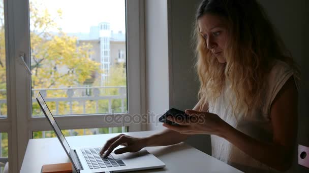 Leuke jonge vrouw praten met vrienden via mobiele telefoon terwijl u werkt op een laptop, en vinden nuttige informatie voor te bereiden op het seminar zittend thuis — Stockvideo