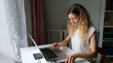 Evde otururken seminer için hazırlamak için cep telefonu aracılığıyla arkadaşlarınızla bir dizüstü bilgisayar ve bulmak yararlı bilgiler çalışırken sevimli genç kadın söz