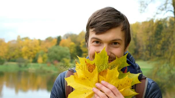 Giovane gay uomo scherzare intorno e hamming ridere e fare selfie con autunno foglie su bianco il moderno smartphone in un parco . — Video Stock