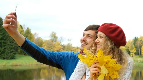 Aşk, teknoloji, ilişki, Aile ve insan kavramı - selfie yanında sonbahar Park smartphone alarak akçaağaç yaprağı ile çift gülümseyen — Stok video