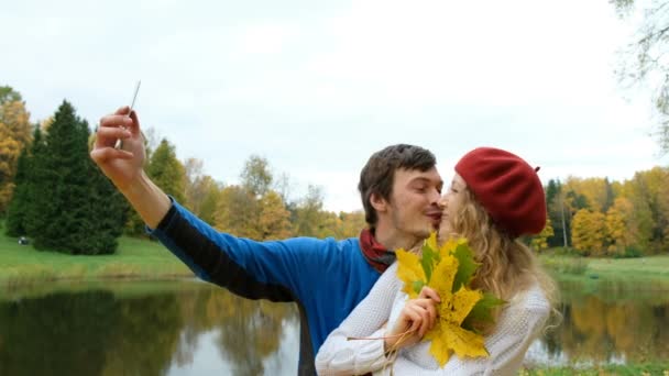 Amor, tecnología, relación, familia y concepto de personas - pareja sonriente con hoja de arce tomando selfie por teléfono inteligente en el parque de otoño — Vídeos de Stock